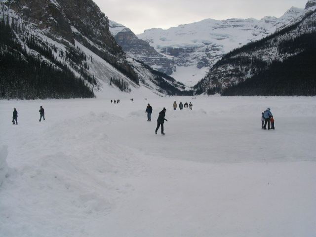 Skaters on frozen Lake Louise below snowy mountains