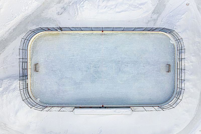 Aerial view of an empty snowy outdoor ice rink with boards